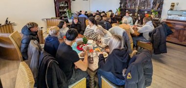 I et stort lokale på Café Grenzenlos sidder elever fra 9. og 10. klasse sammen med ældre deltagere i initiativet "Bedstemødre mod højre". Folk er spredt rundt i lokalet ved flere borde og sidder over for hinanden i små diskussionsgrupper. Nogle sidder på stole ved borde med drikkevarer og tallerkener, andre i sofaer langs væggen. I baggrunden kan man se andre grupper, som også taler med hinanden.