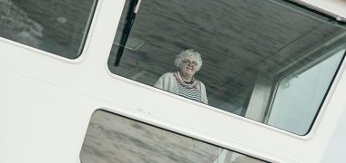 La imagen muestra a la directora Ursula Steuer detrás de los grandes cristales frontales del puente de un transbordador. Fotografiada desde abajo, parece pequeña frente a las superestructuras blancas del barco, mientras mira hacia el exterior con una sonrisa.
