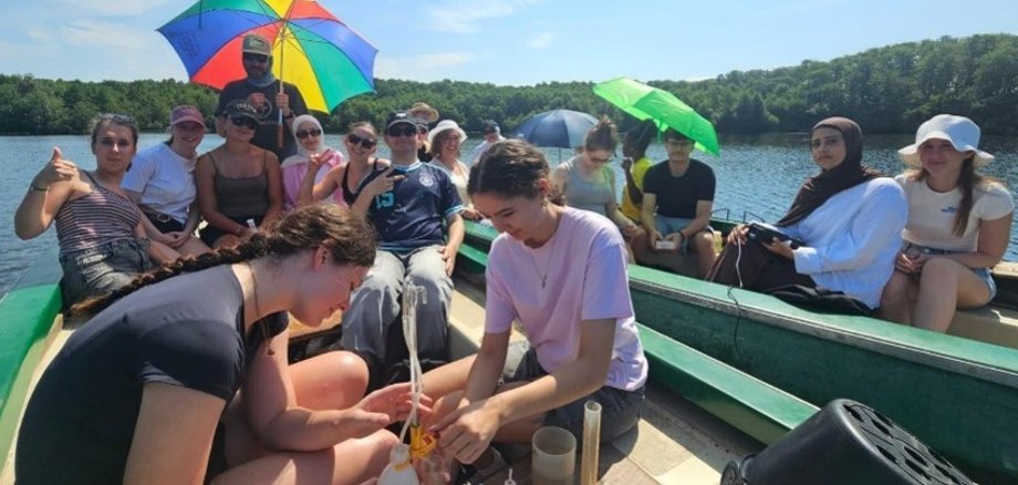 Lors d'une sortie scolaire, deux adolescents sont assis dans un petit bateau sur un lac et préparent des appareils de mesure en vue d'une analyse de l'eau.