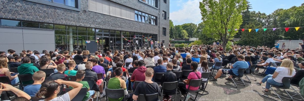 Les élèves sont assis ensemble dans la cour de l'école et regardent la scène.