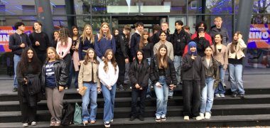 Scambio scuola completa Gronau e Stedelijk Lyceum Enschede Zuid Un folto gruppo di alunni dell'Istituto Comprensivo di Gronau e dello Stedelijk Lyceum Enschede Zuid si trova insieme sui gradini di fronte al cinema Cinetech di Gronau. I giovani posano per una foto di gruppo dopo una discussione comune sul tema della sostenibilità. La facciata in vetro del cinema con la scritta illuminata "Cinetech" è visibile sullo sfondo.