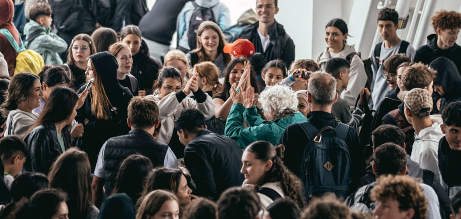 페리 선실 안에는 수많은 여학생들과 교사들이 서로 바짝 붙어 서 있다. 사진 중앙에서는 슈테우어 선생님이 여러 청소년들과 함께 춤을 추고 있다. 많은 여학생들이 미소를 짓거나 그 장면을 지켜보거나 이야기를 나누고 있다. 페리는 승객으로 꽉 찬 듯 보이며, 분위기는 즐겁고 활기차다.