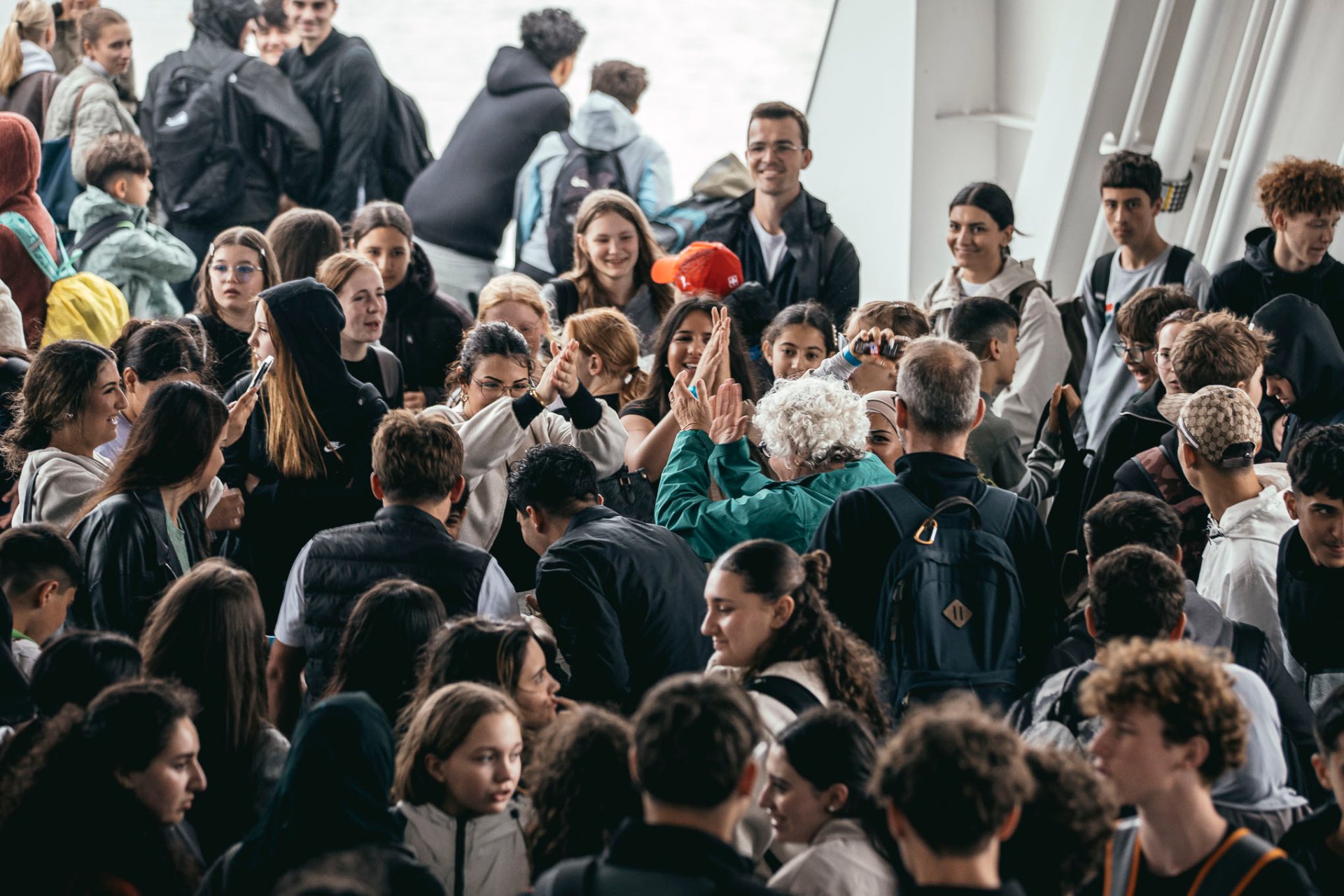 Binnen in de veerboot staan talrijke leerlingen en docenten dicht bij elkaar. In het midden van de foto danst mevrouw Steuer samen met een aantal jongeren. Veel leerlingen glimlachen, kijken toe of zijn in gesprek. De veerboot lijkt goed gevuld en de sfeer is vrolijk en uitgelaten.
