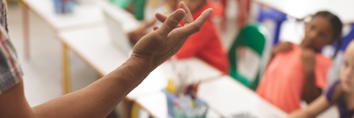 Grande plano do braço do professor contra um borrão de crianças sentadas na sua cadeira numa sala de aula na escola
