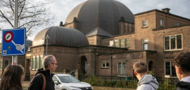 Besök i synagogan i Enschede - 2025 En lärare och flera elever från årskurs 9/10 i Gronau grundskola står på en gata och tittar mot den stora kupolsynagogan i Enschede.
