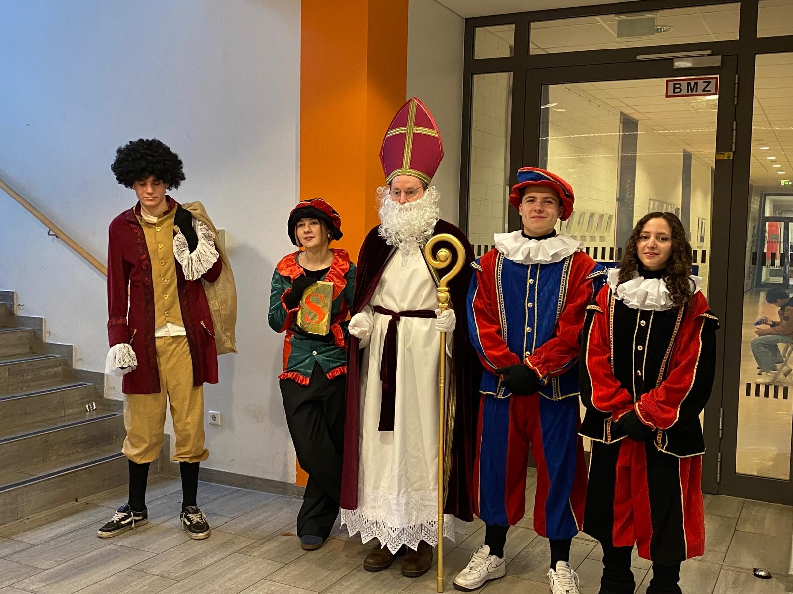 格罗瑙综合学校的走廊上站着一位打扮成 Sinterklaas 的人，他头戴司铎和十字架，旁边还有四位打扮成传统同伴的学生。他们穿着五颜六色的服装，准备迎接五年级学生的来访。